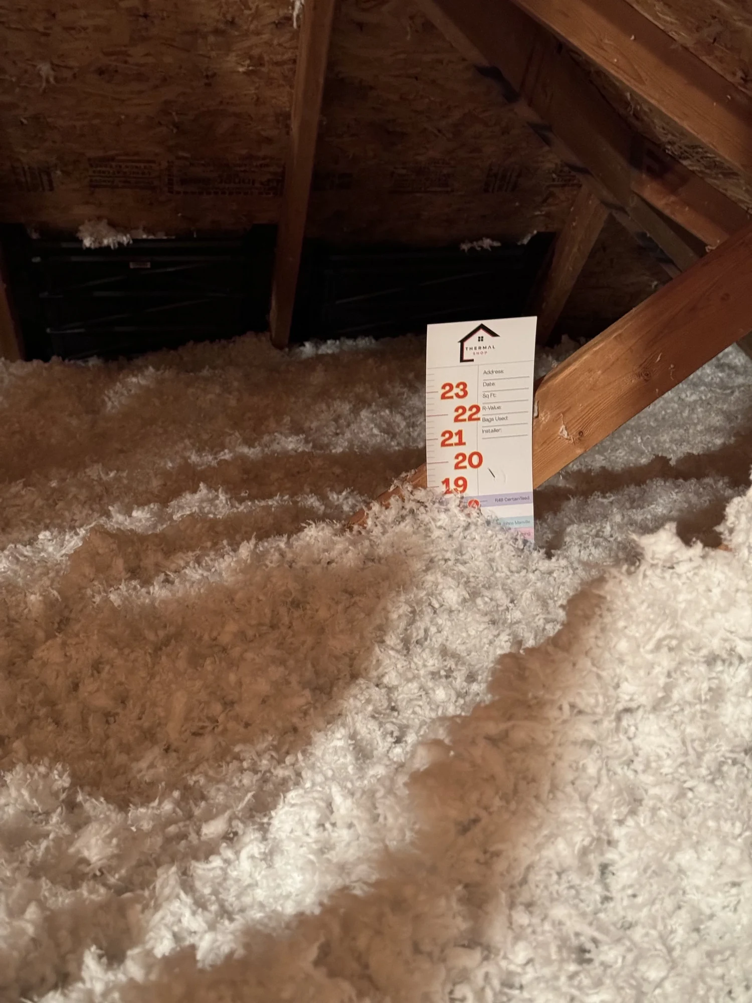 Depth marker card standing in freshly blown white loose fill in an attic