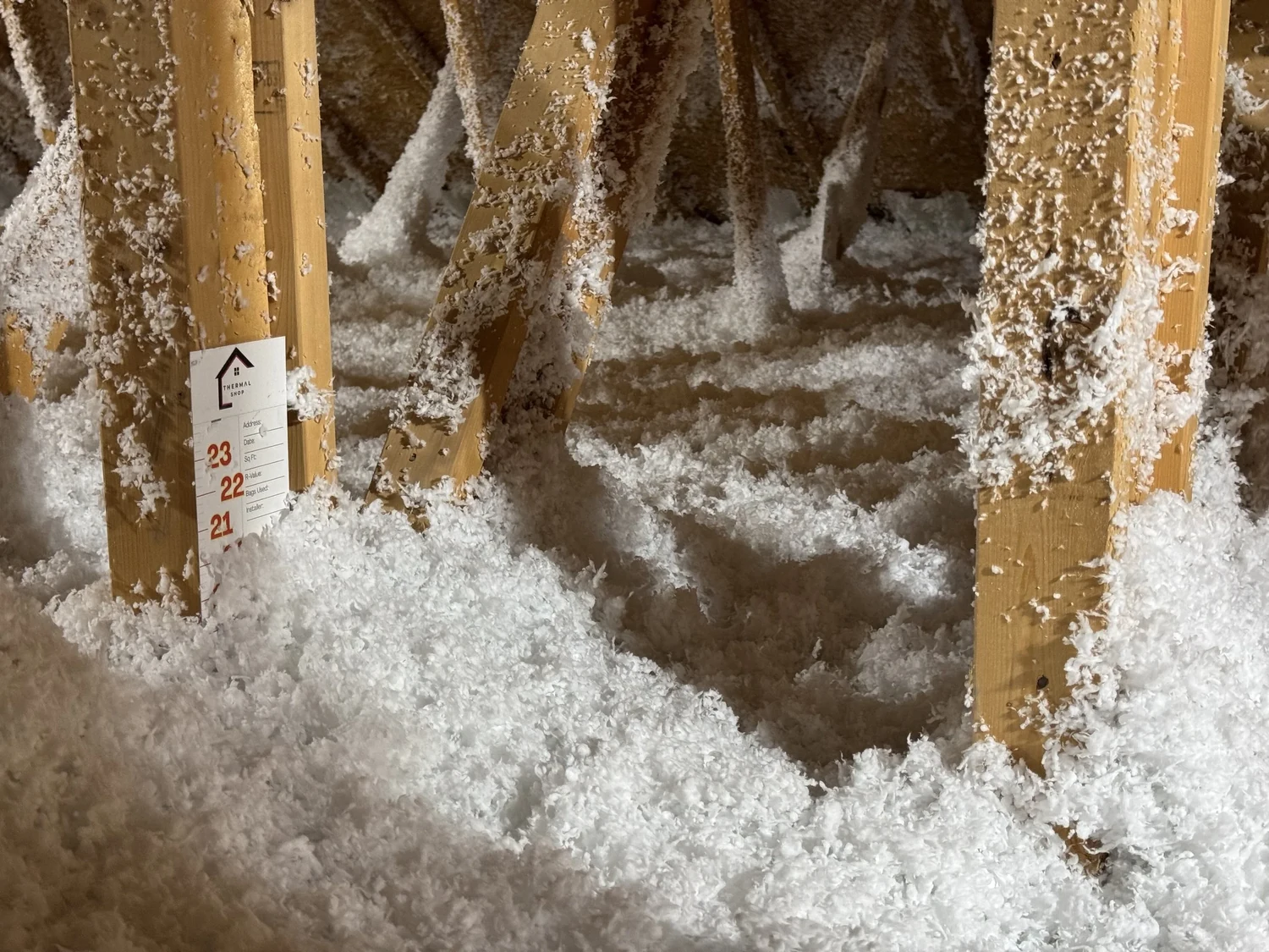 White loose fill blown between truss webs, with a depth marker card on a truss