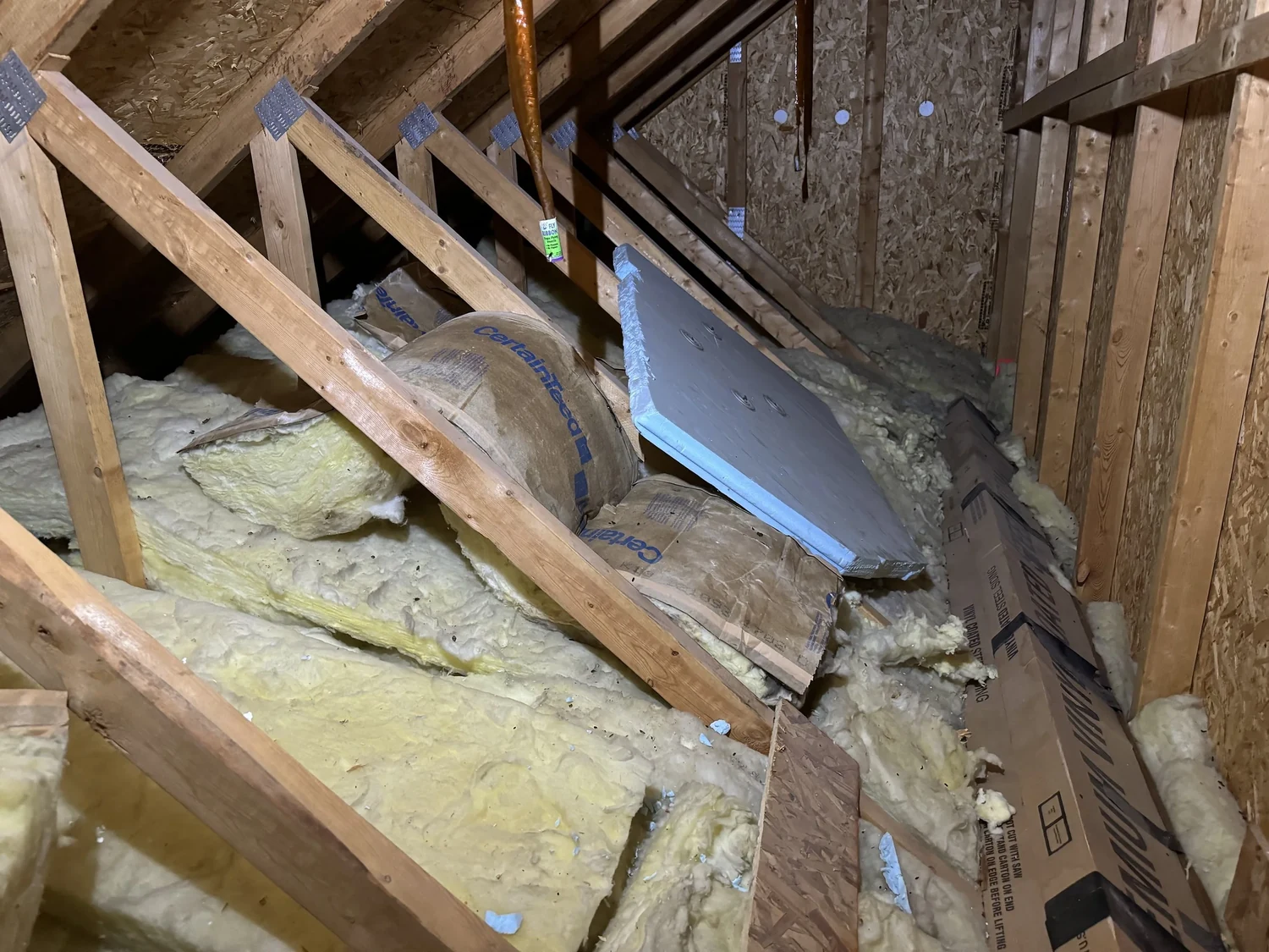 Yellow fiberglass batts pulled out of place and bunched between attic trusses