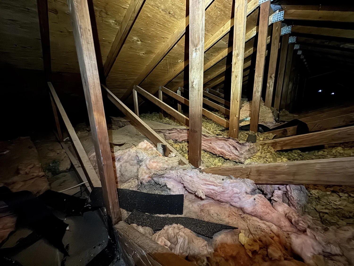 Long attic with disturbed pink batts and bare spots between the trusses