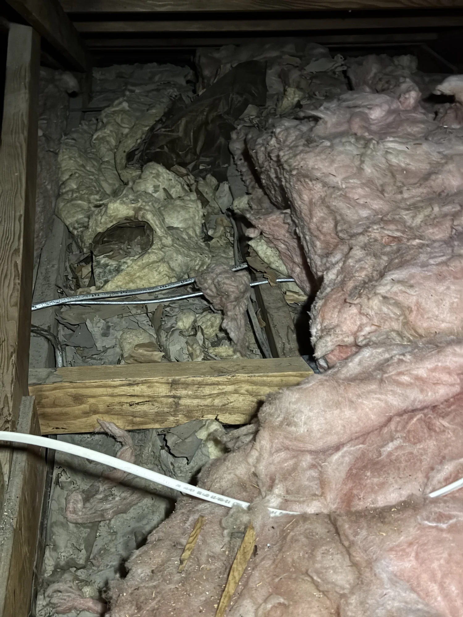 Pink fiberglass batts matted and torn around wiring in an attic