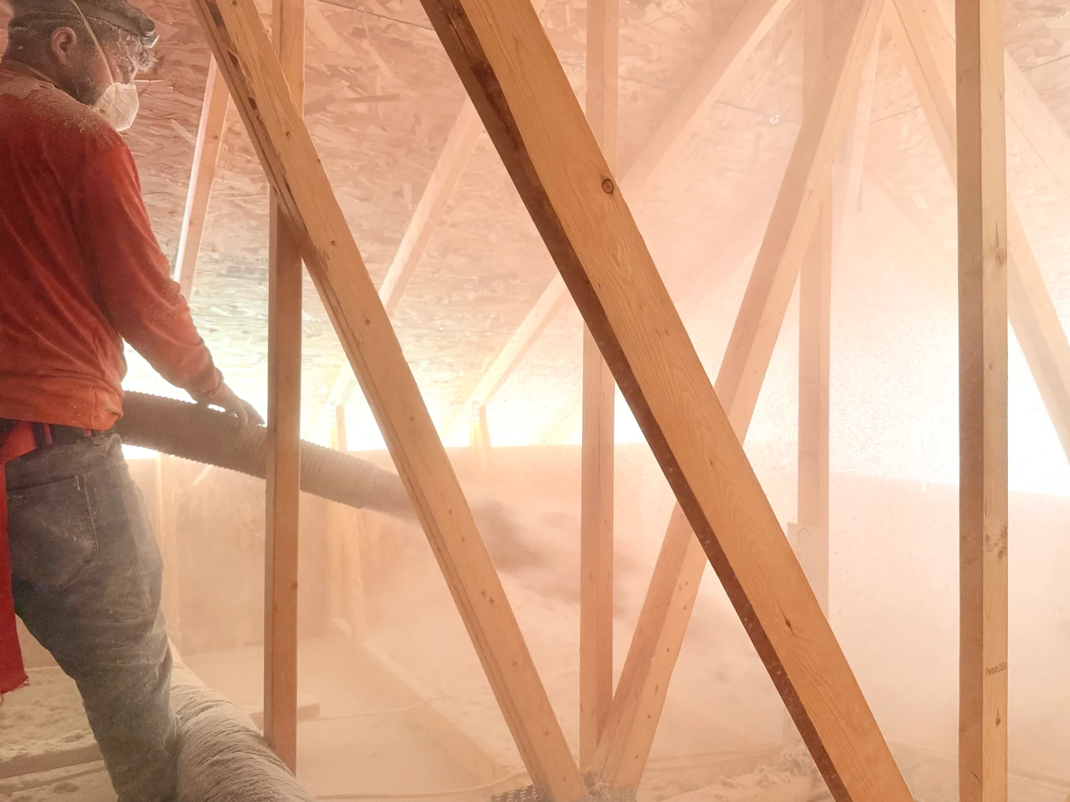 Installer guiding the insulation hose between attic trusses as loose fill blows across the floor