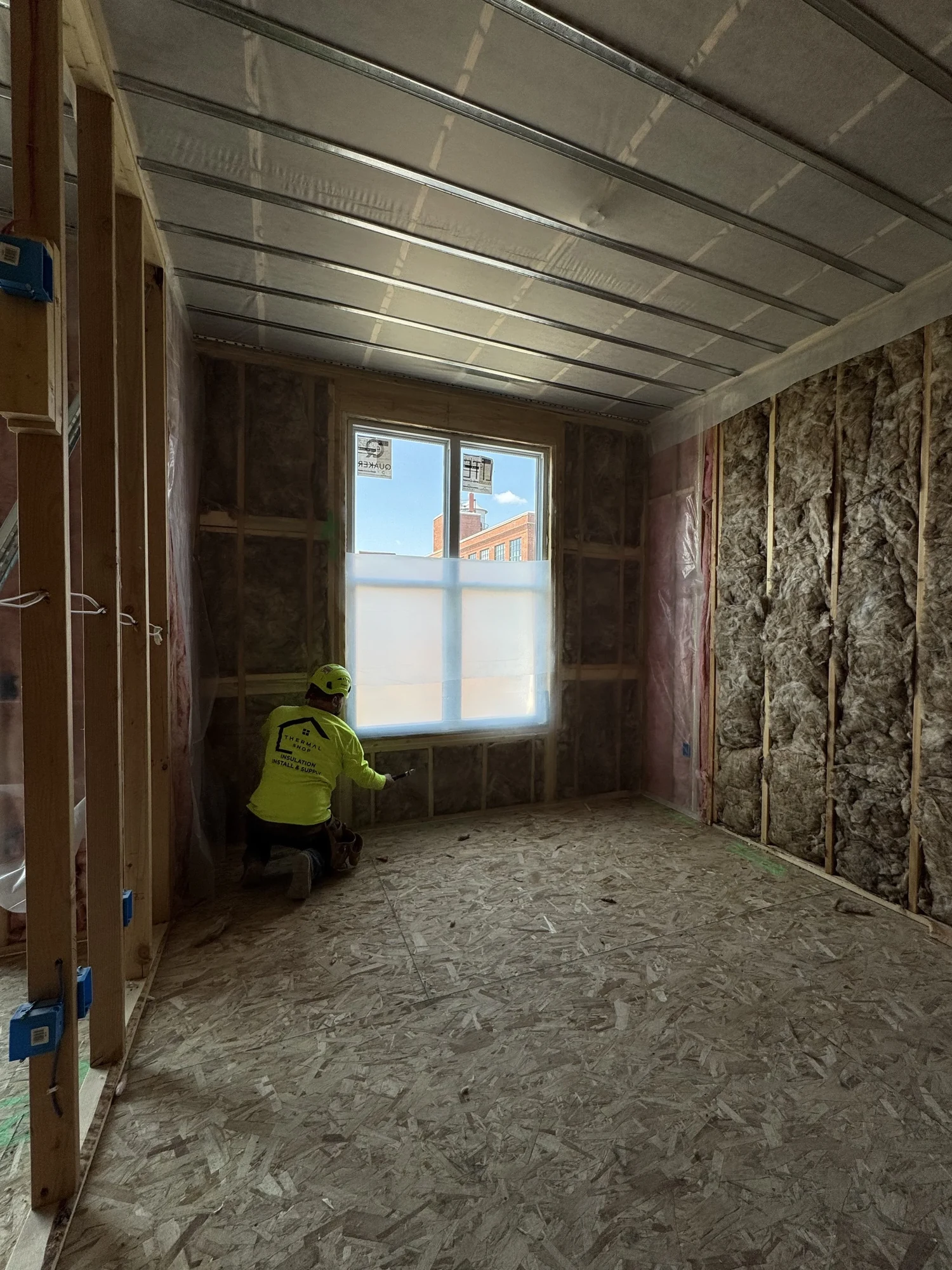 Installer kneeling to fit fiberglass batts under a window in a framed room
