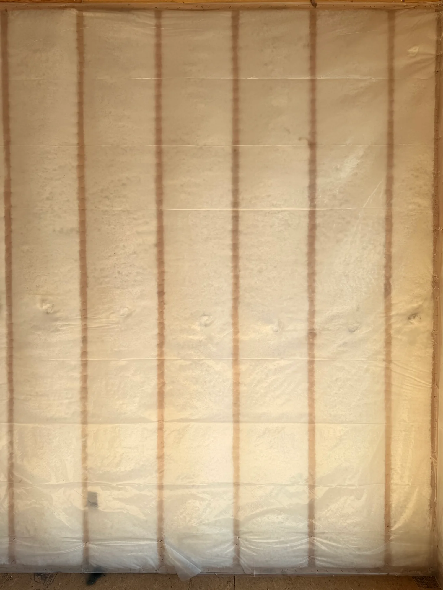 Close view of a wall blown full of fiberglass behind netting, the netting stapled along each stud