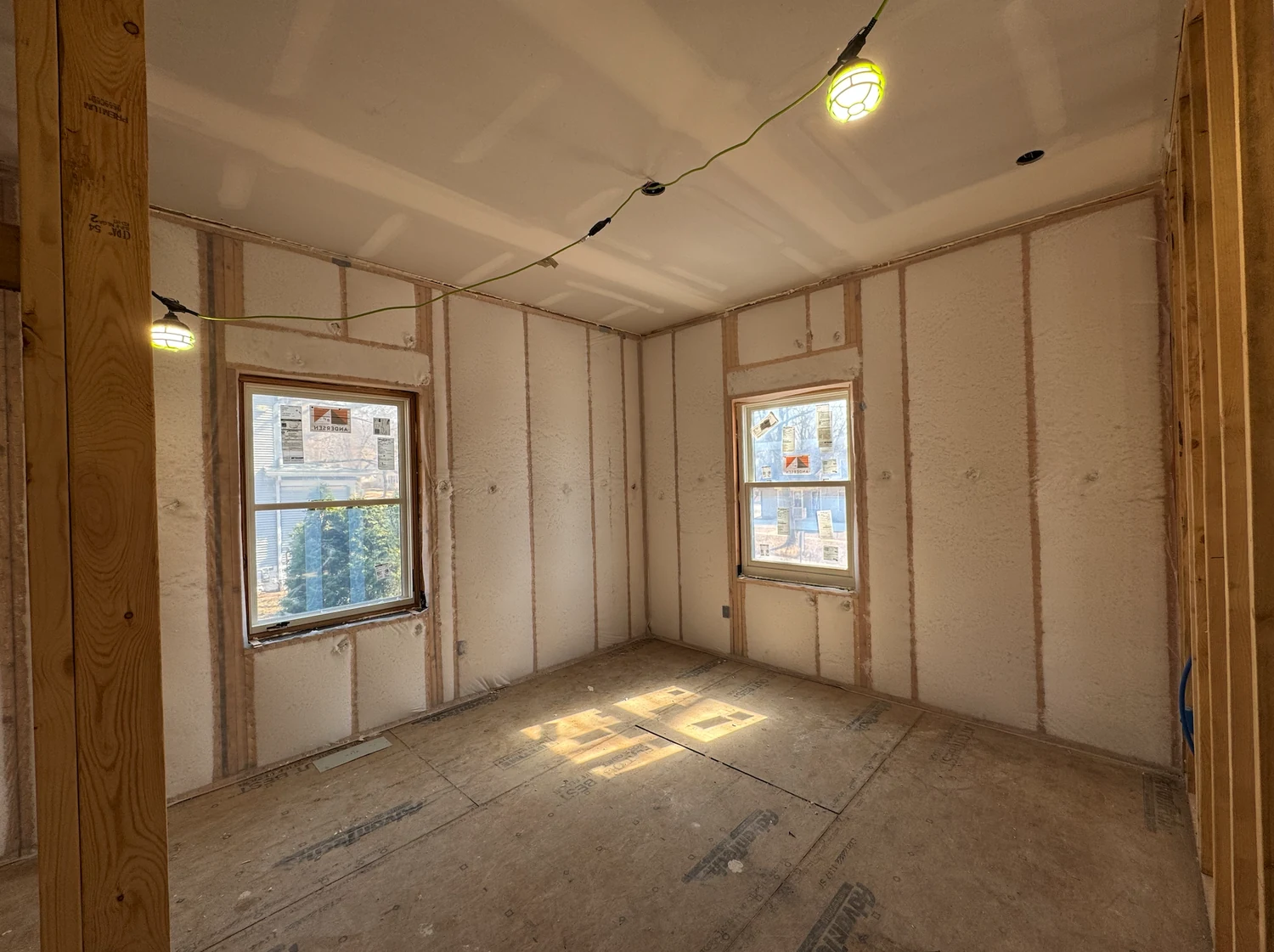 Bedroom with fiberglass blown behind netting on every wall and a work light hanging from the ceiling