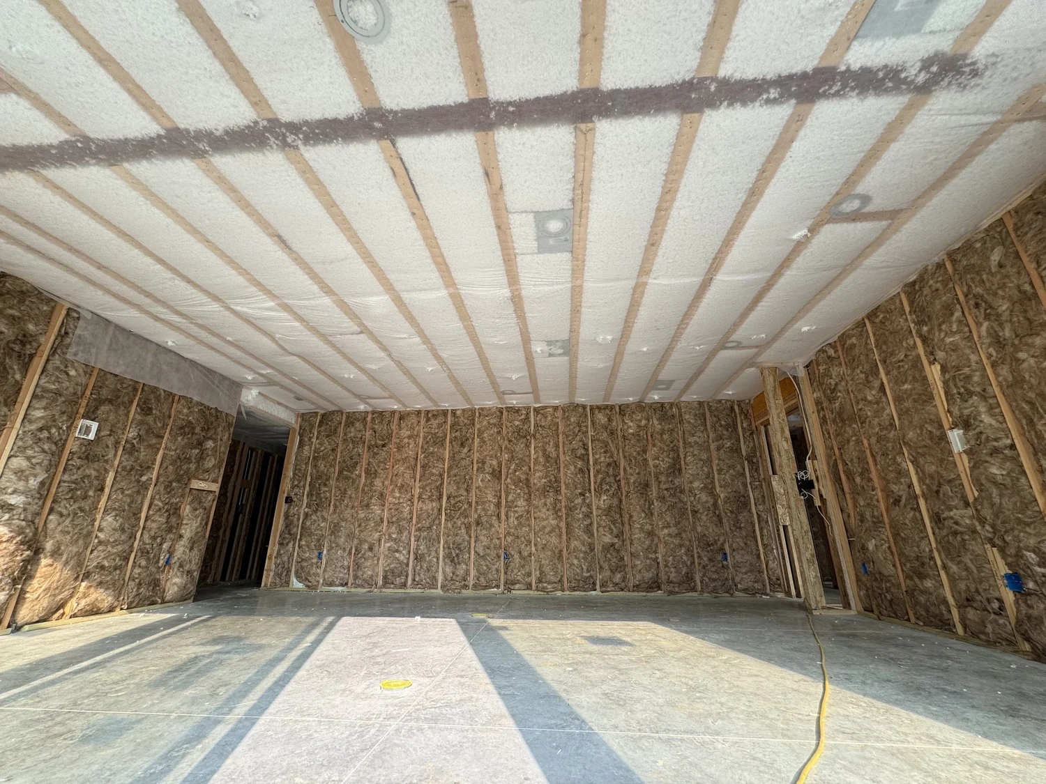 Room with a netted, blown ceiling overhead and fiberglass batts in the walls