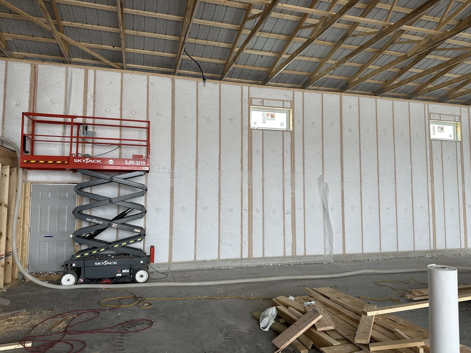 Pole building interior with white netting across the insulated walls and a scissor lift
