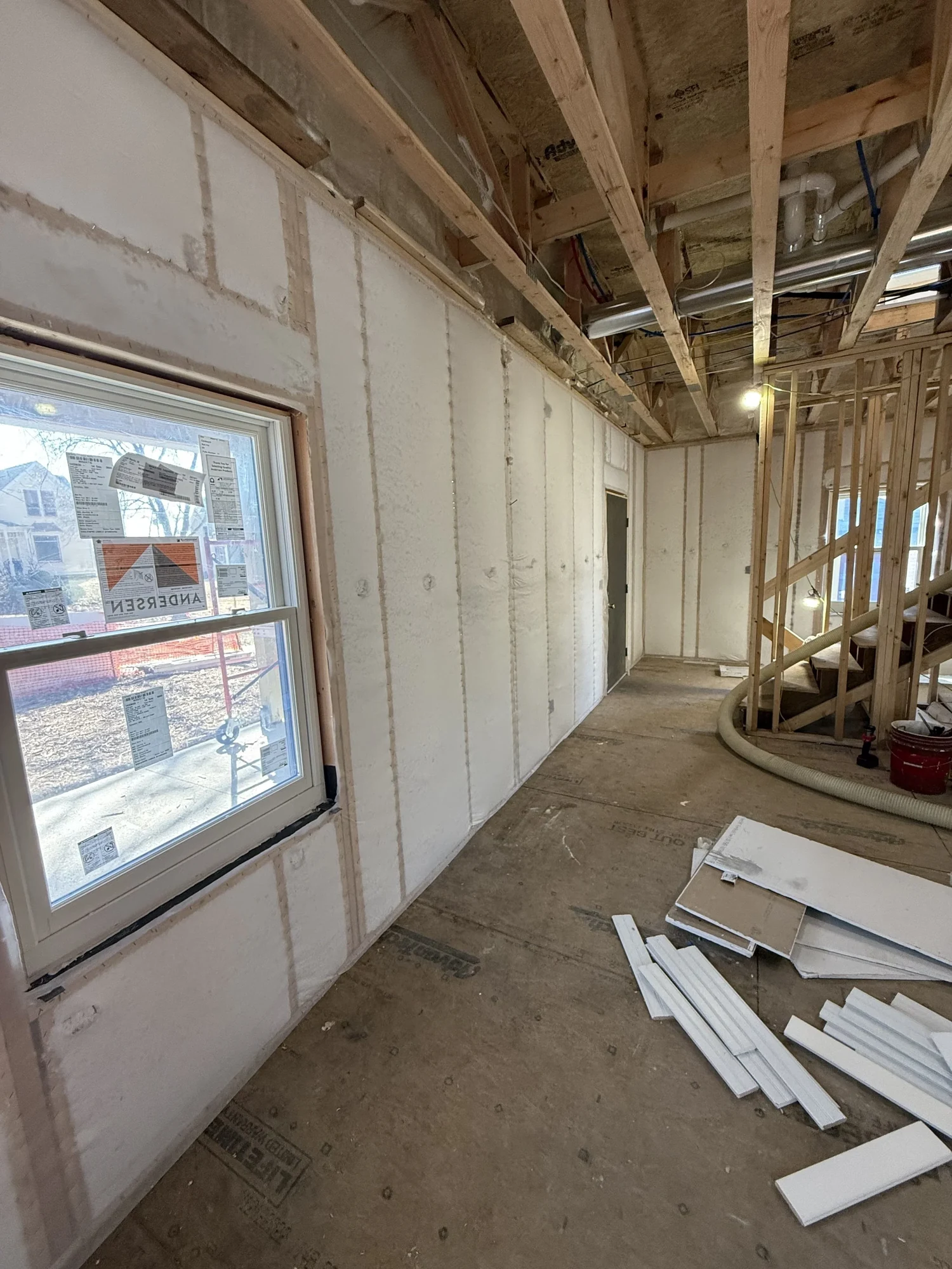 Wall of fiberglass behind netting beside a window, with trim scraps on the floor