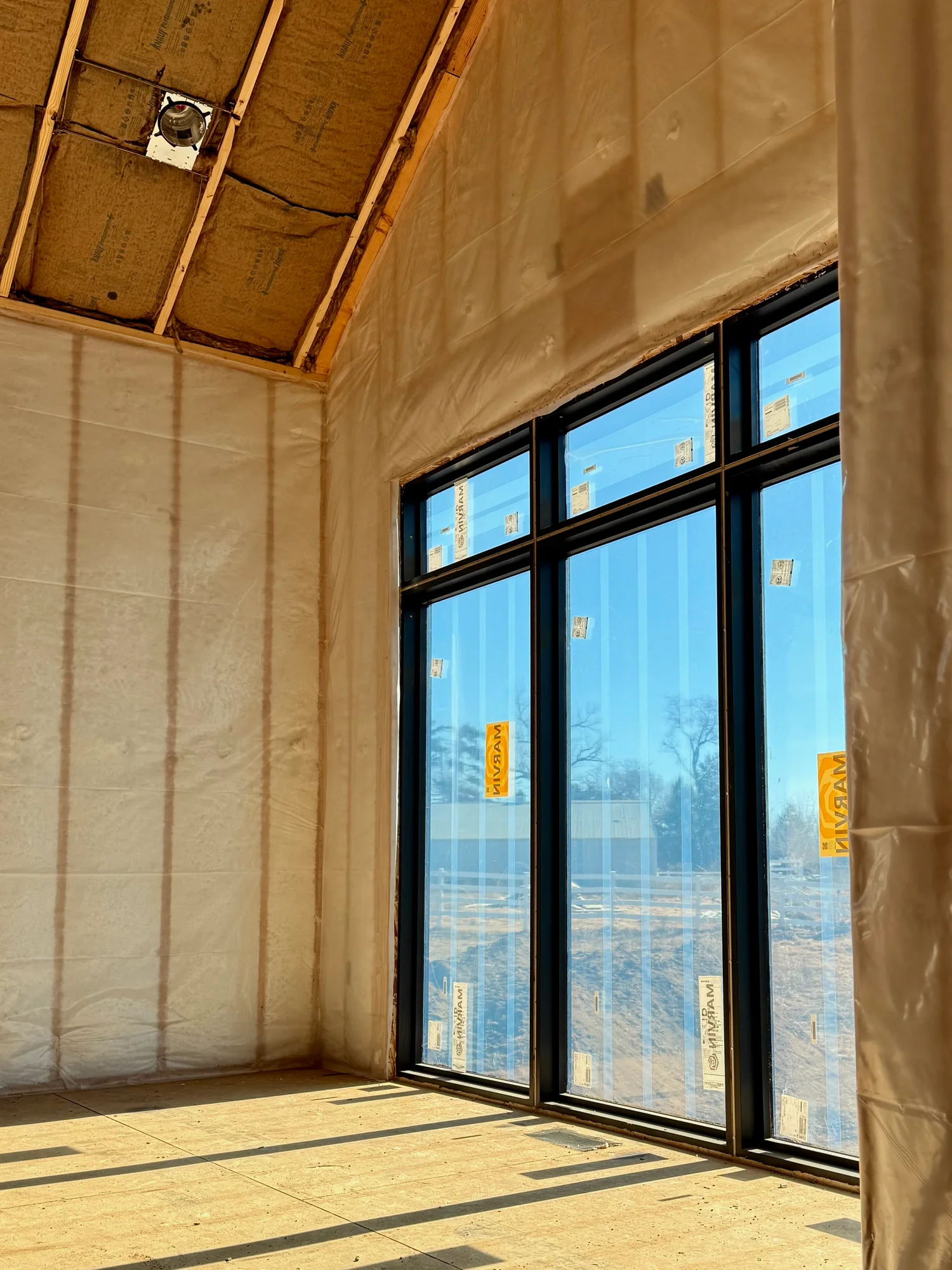 Blown-in fiberglass held behind netting in a vaulted room with tall windows, before drywall