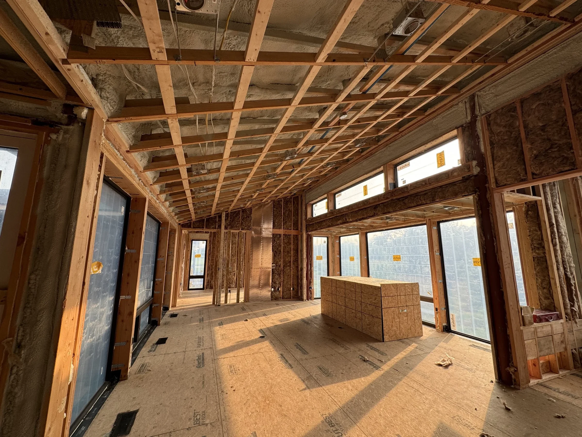 Framed great room in a custom home under construction, with insulation in the walls and ceiling and wrapped windows along one side