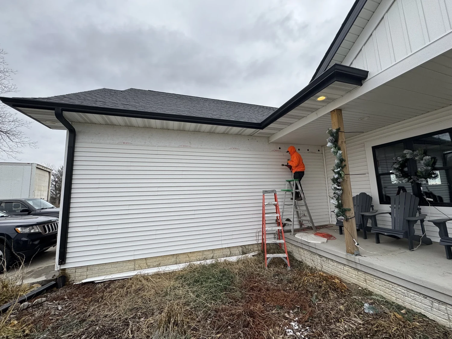 Installer on a ladder at the corner of a house beside the front porch