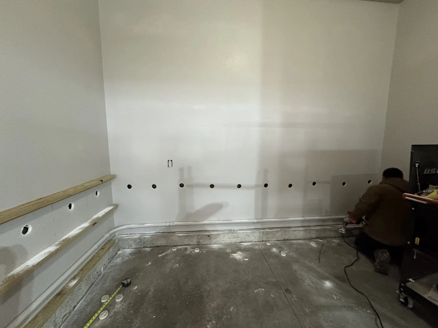 Installer kneeling at a finished garage wall lined with access openings