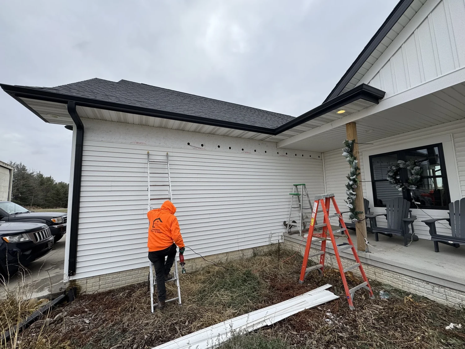 Installer on a ladder at a sided wall with a row of access openings under the eave