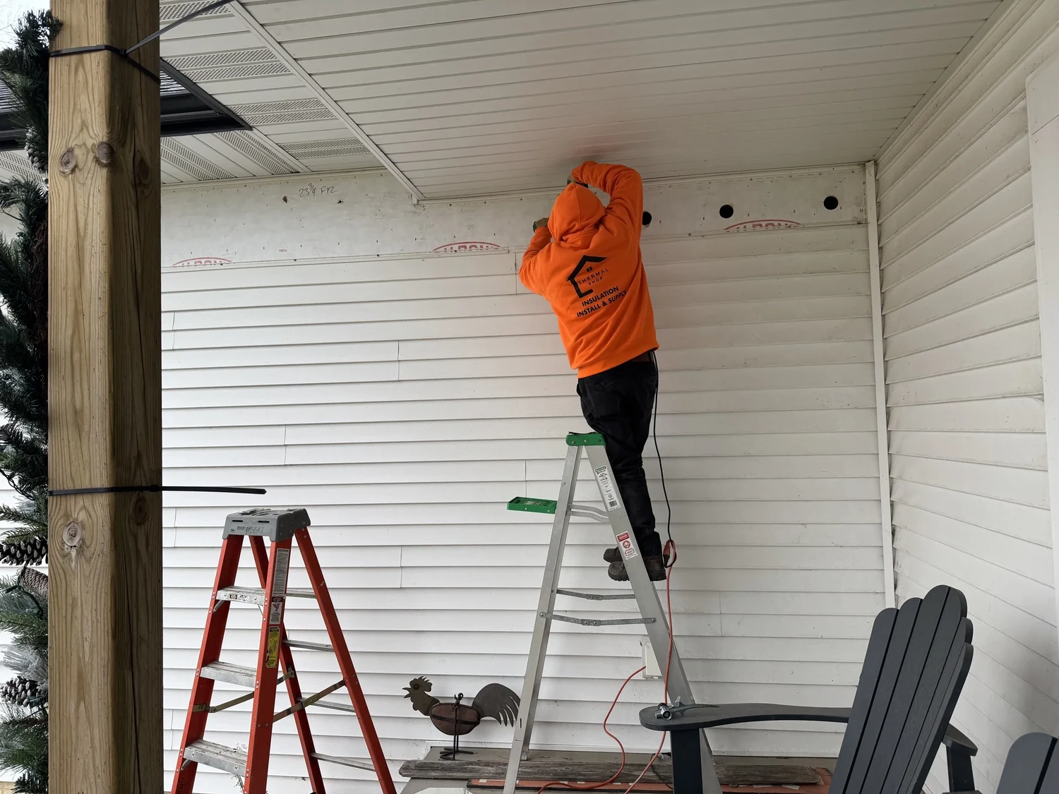 Porch wall with a row of access openings near the ceiling and an installer on a stepladder