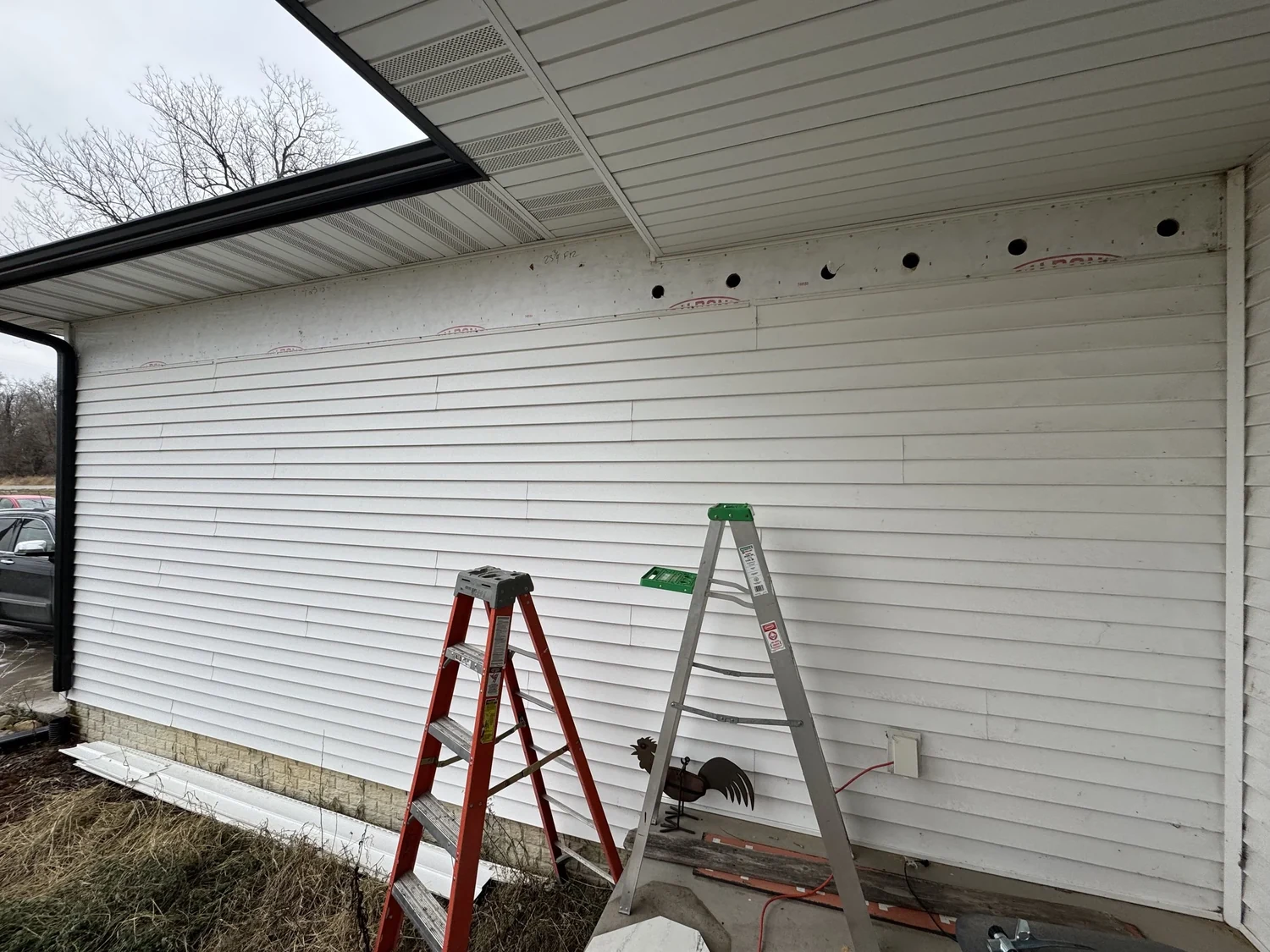 Vinyl-sided wall with a line of access openings near the top and two ladders against it