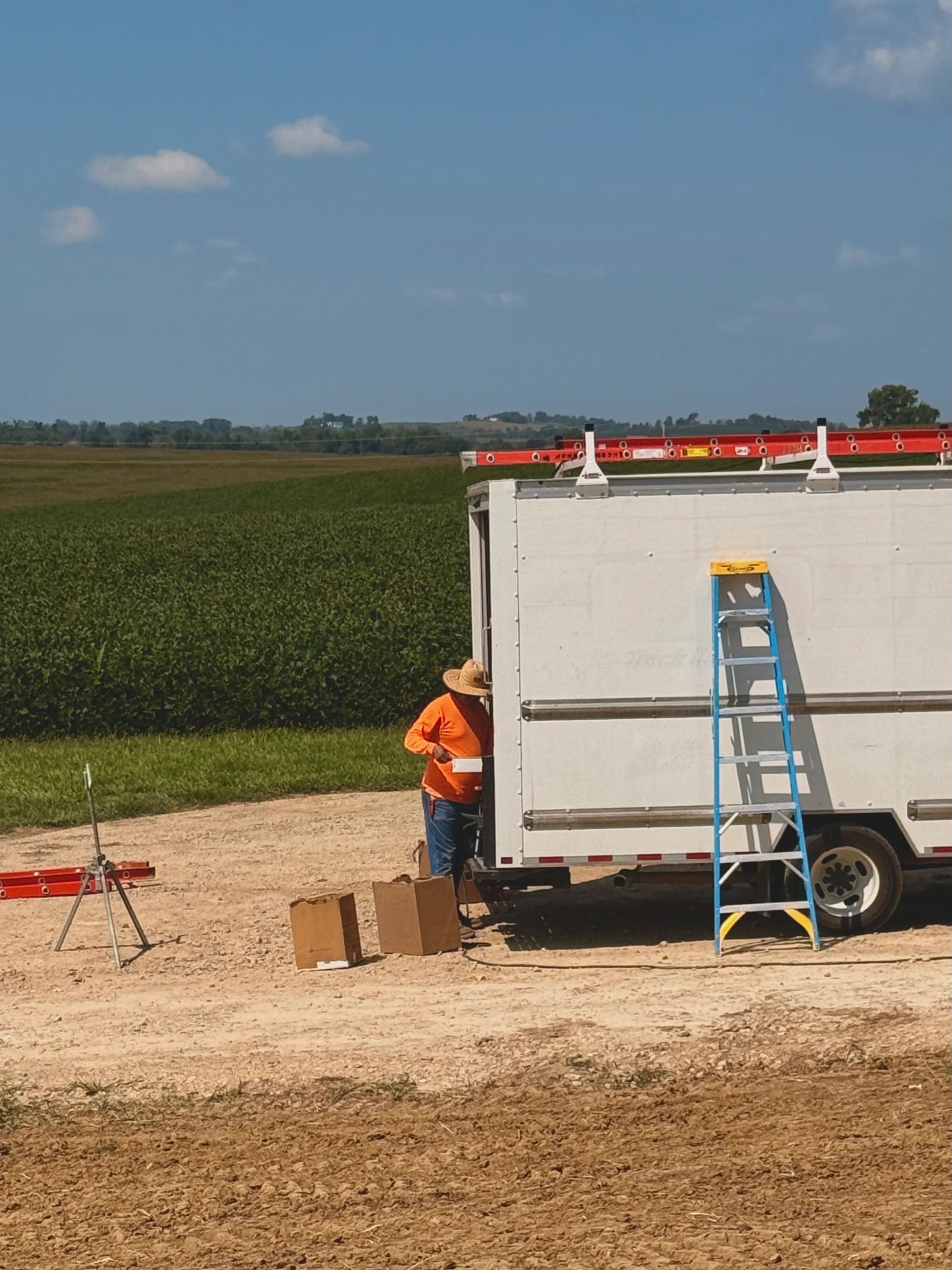 The installer guiding the forming gutter with one hand as it feeds out of the truck, cornfield and gravel drive behind
