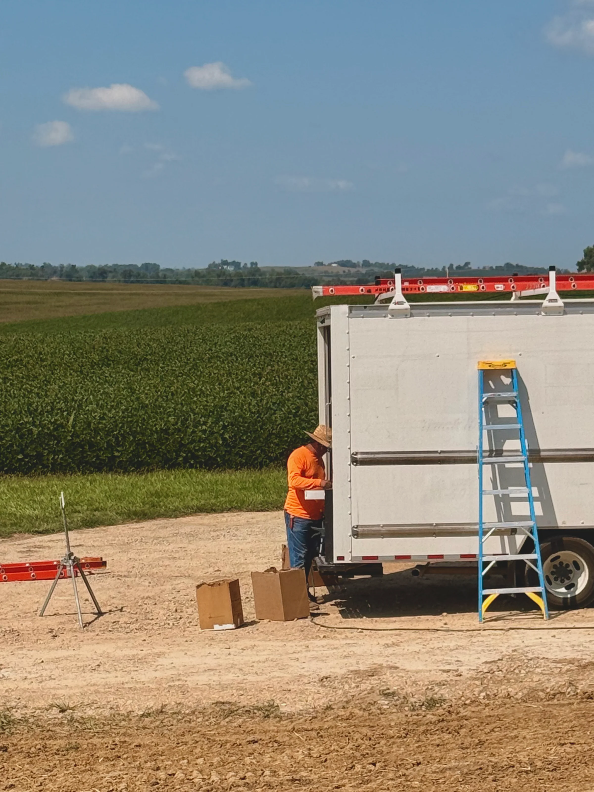 The installer leaning over the gutter as it runs out of the machine, a blue stepladder against the truck beside him