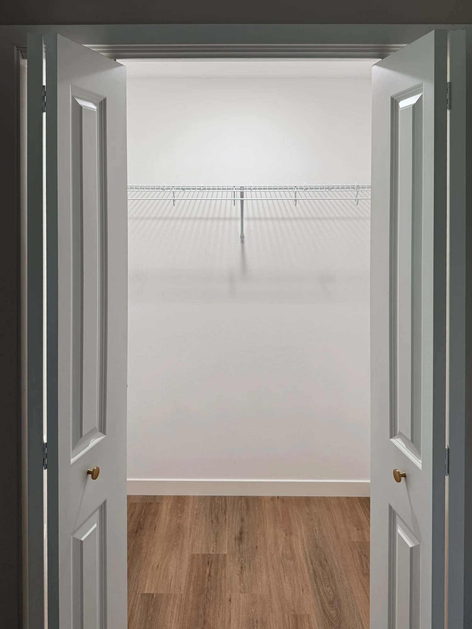 A white wire shelf and hanging rod in a closet framed by open bifold doors