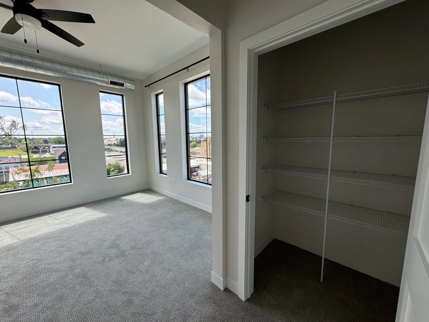 An empty apartment bedroom with tall windows and an open closet lined with wire shelves