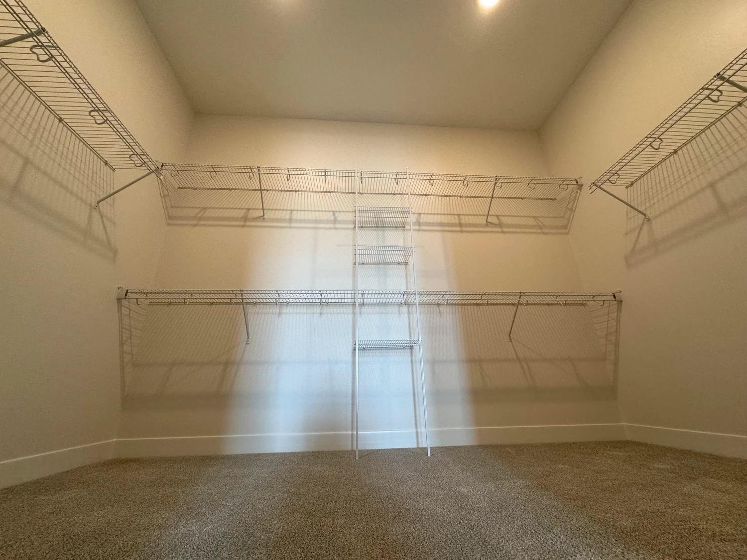 Wire shelving on three walls of an empty walk-in closet, with a shelf tower on the back wall