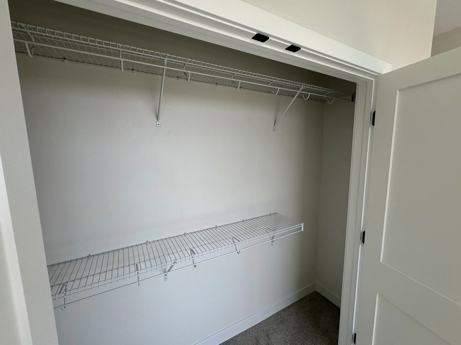Two wire shelves with hanging rods in an apartment closet with double doors