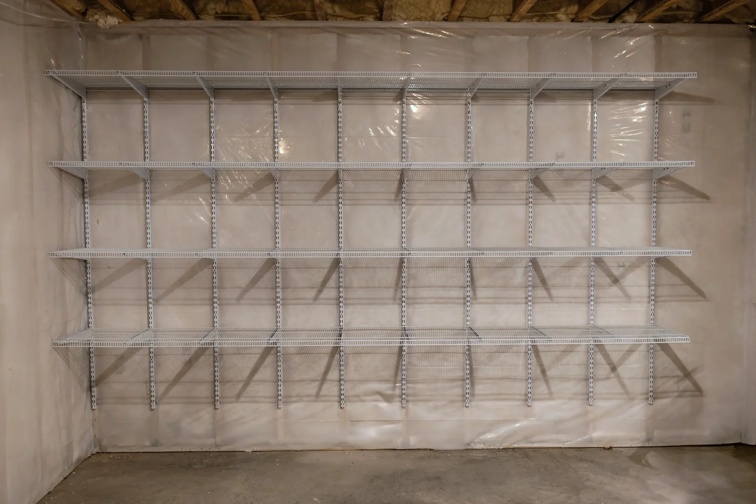 Empty white wire shelves on adjustable standards across an unfinished basement wall