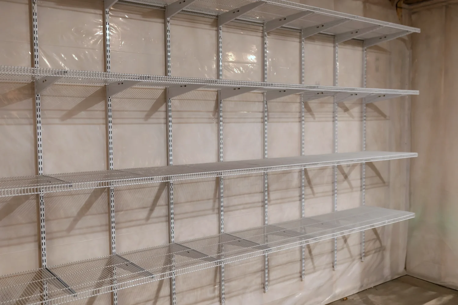 Angled view of empty white wire shelves running along a basement wall