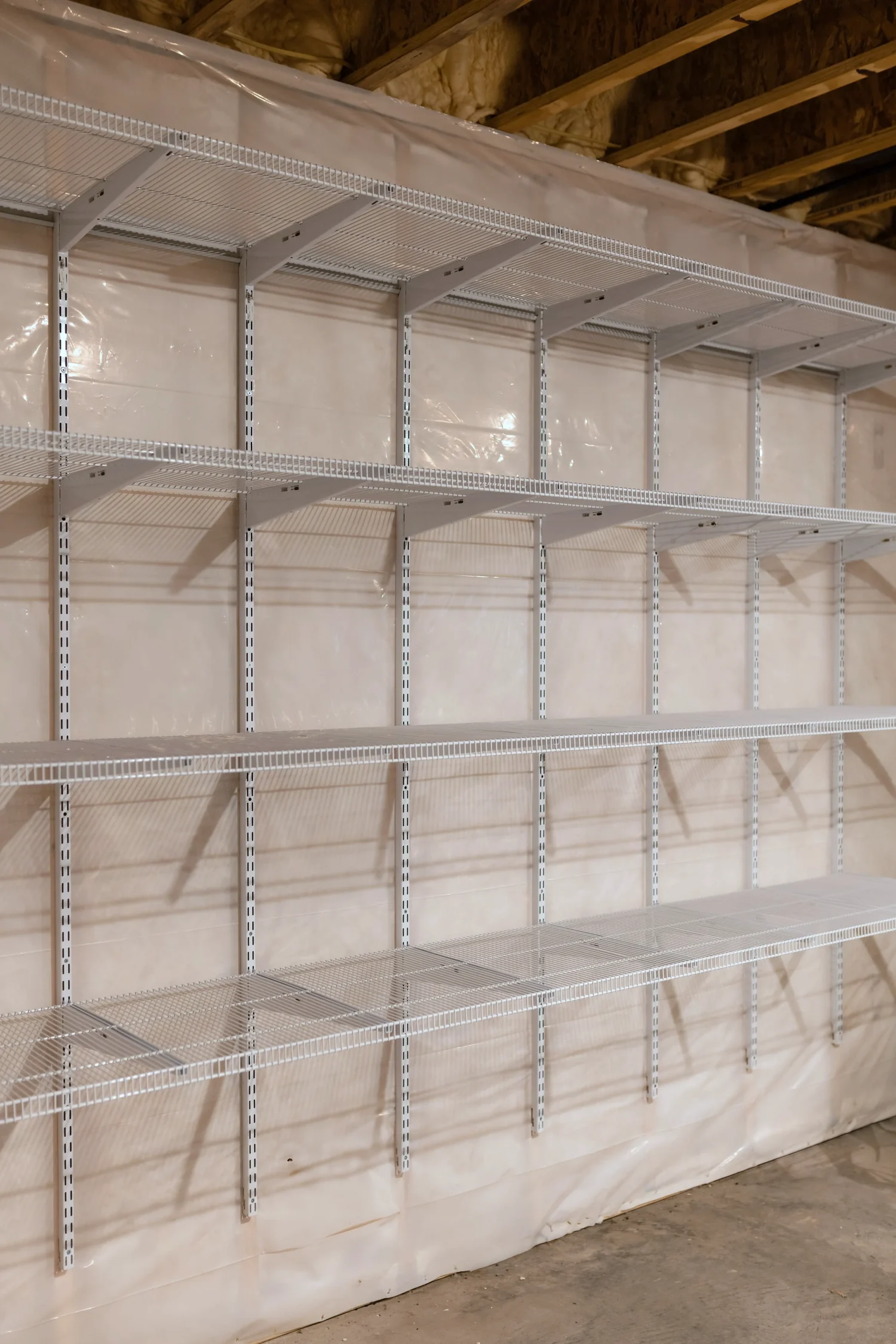 Empty wire shelves on wall standards in the corner of an unfinished basement