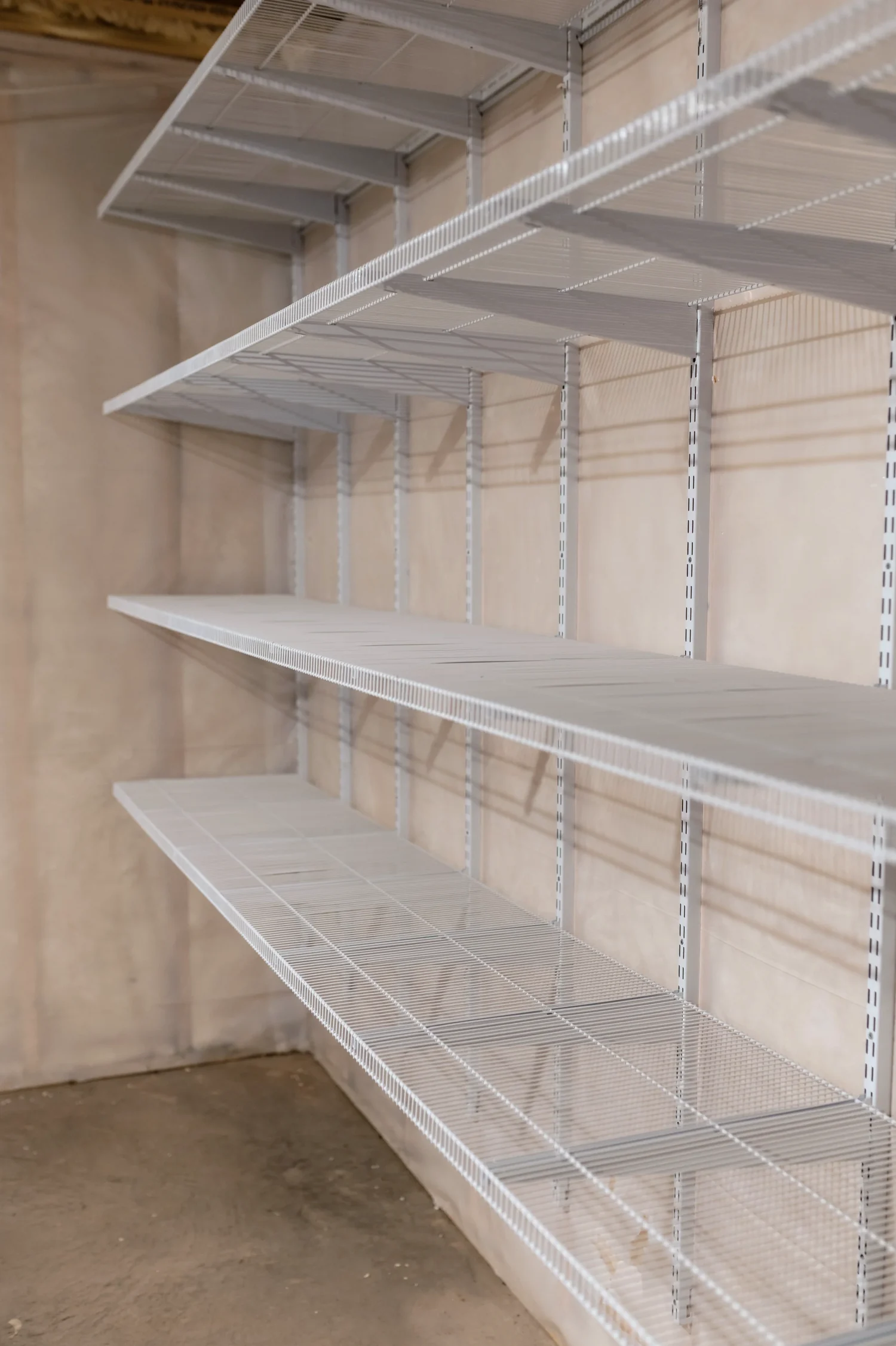 Looking down a run of empty white wire shelves on a basement wall