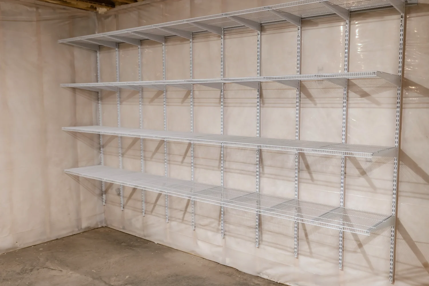 Empty white wire shelves along an unfinished basement wall, seen from the corner