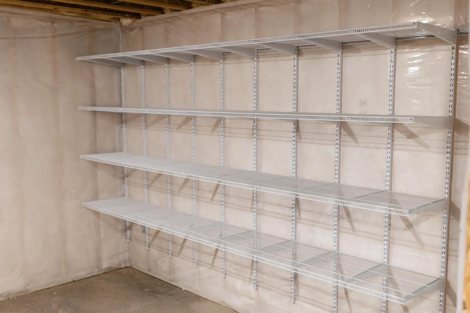 Empty white wire shelves on adjustable standards in a basement, seen from one end