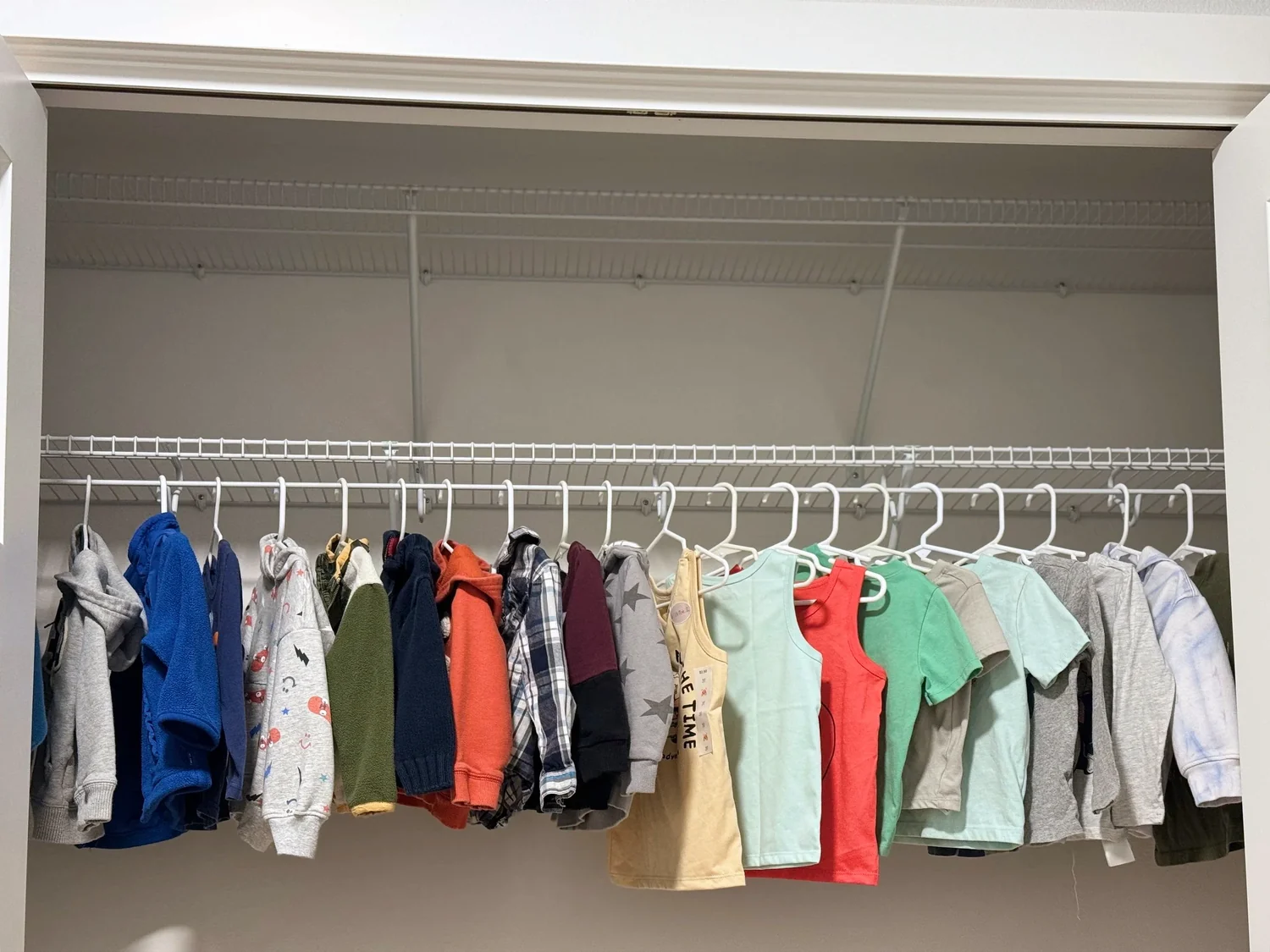 Children's clothes hanging from a wire shelf with a built-in rod in a bedroom closet