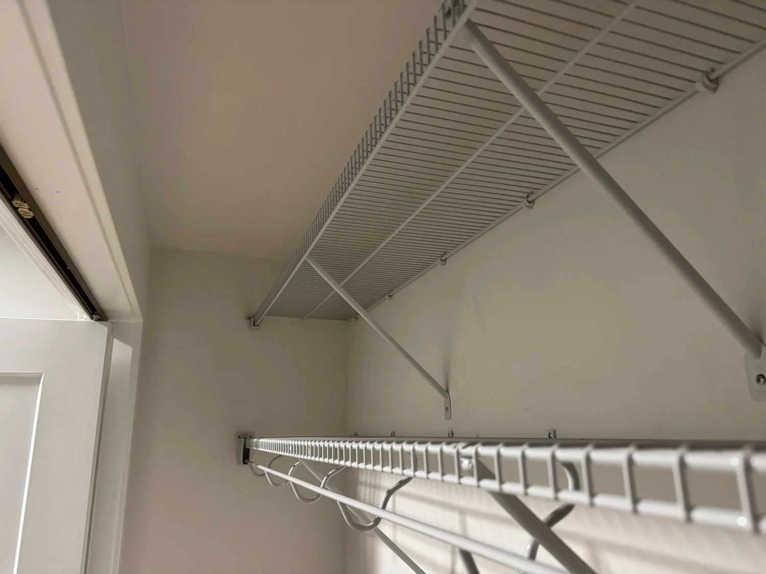 Two wire shelves with hanging rods in the corner of an empty closet