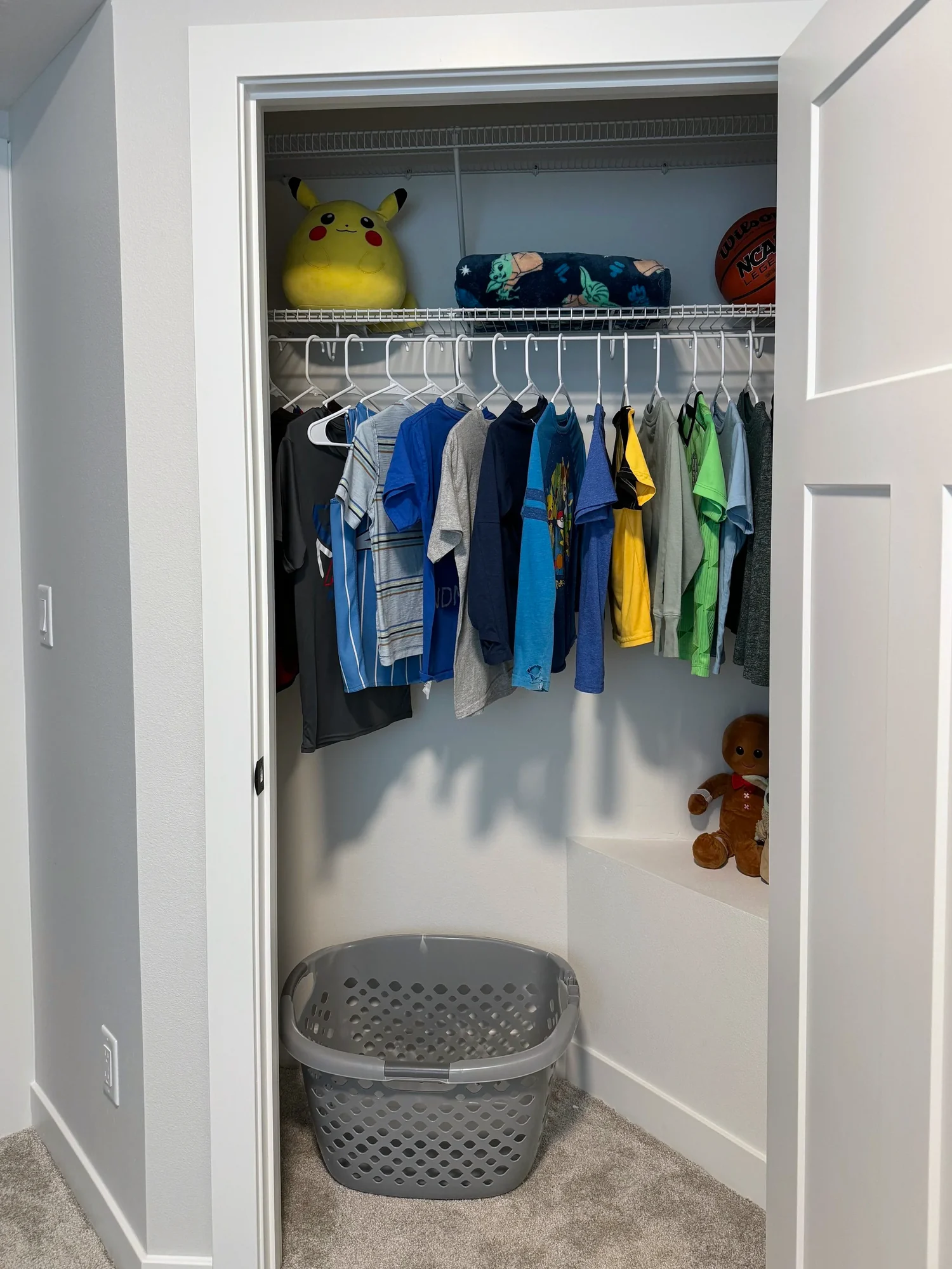 An open closet with clothes hanging from a wire shelf and toys on top