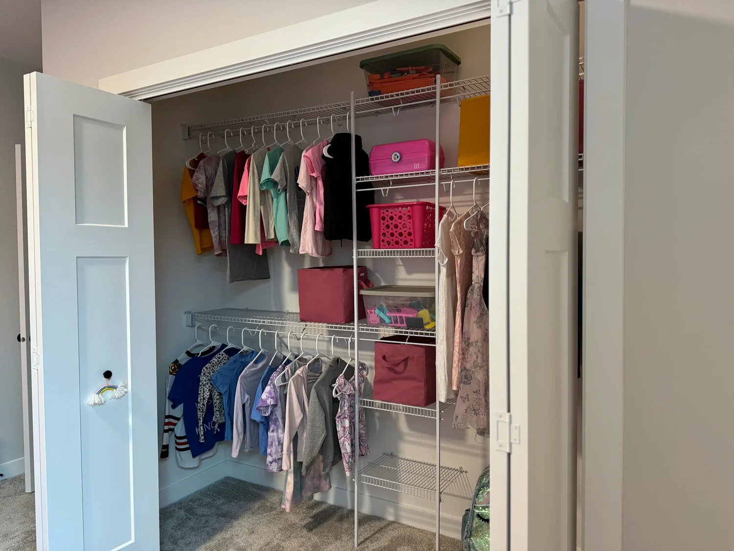 An open closet with children's clothes, bins, and baskets on wire shelving