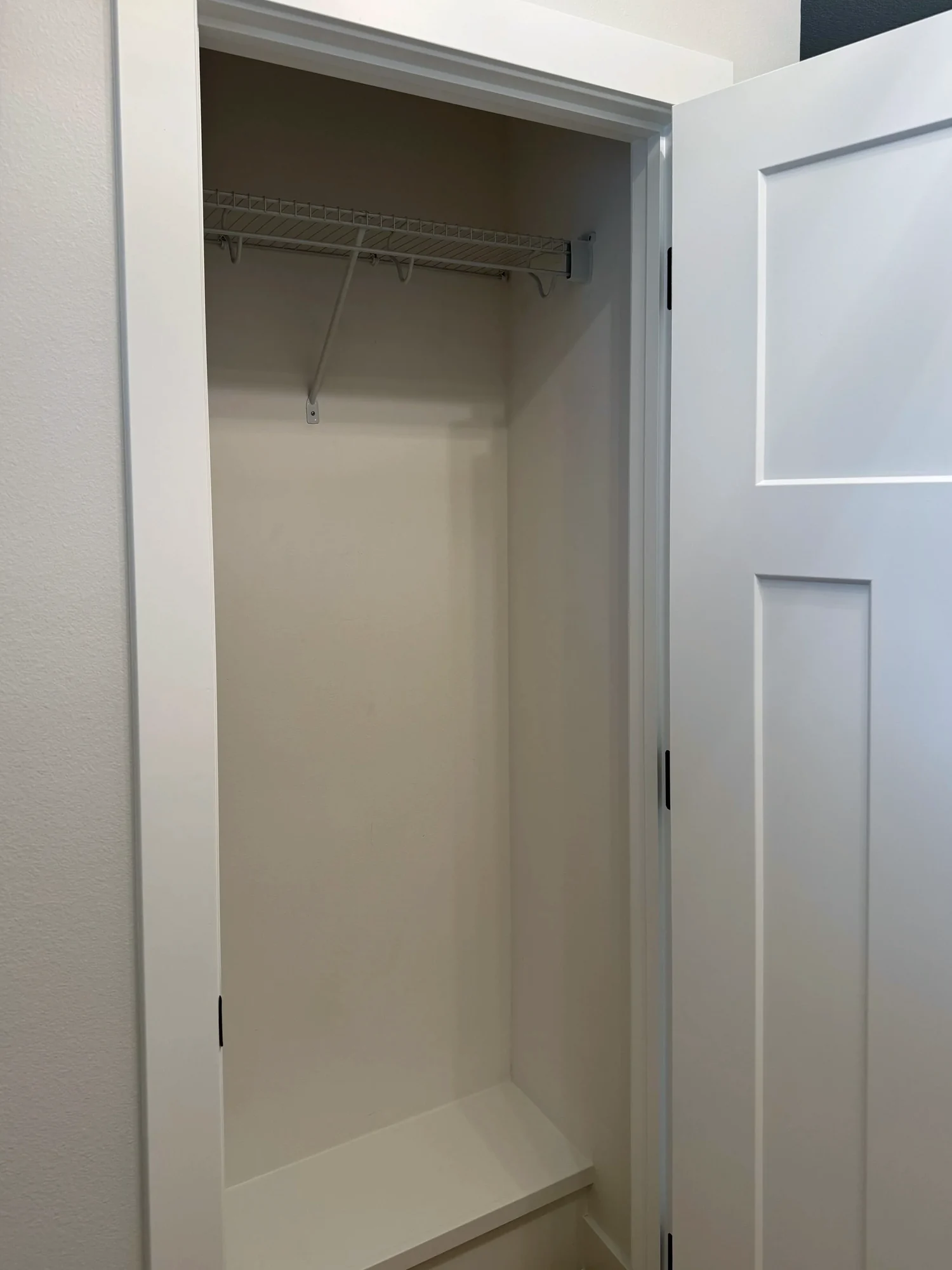 A wire shelf with a hanging rod in an empty closet behind an open door