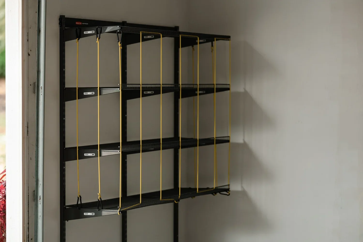 Close view of an empty ball rack with yellow bungee cords on gunmetal garage rails