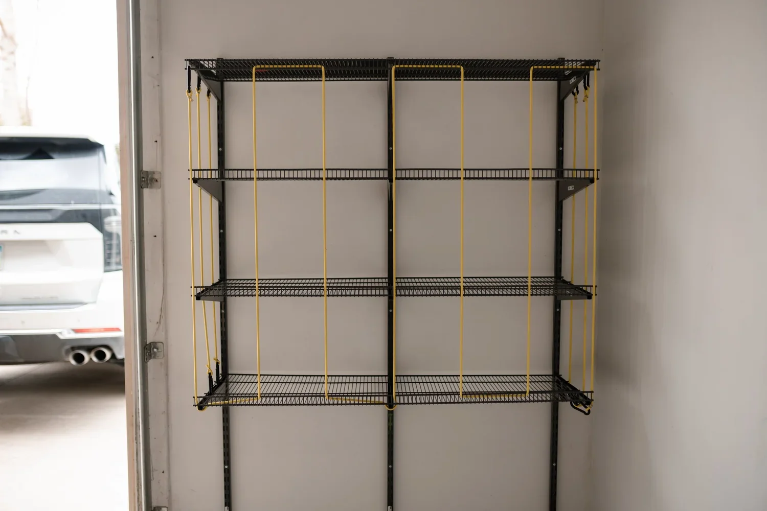 An empty ball rack with yellow bungee cords on gunmetal rails, next to a parked car