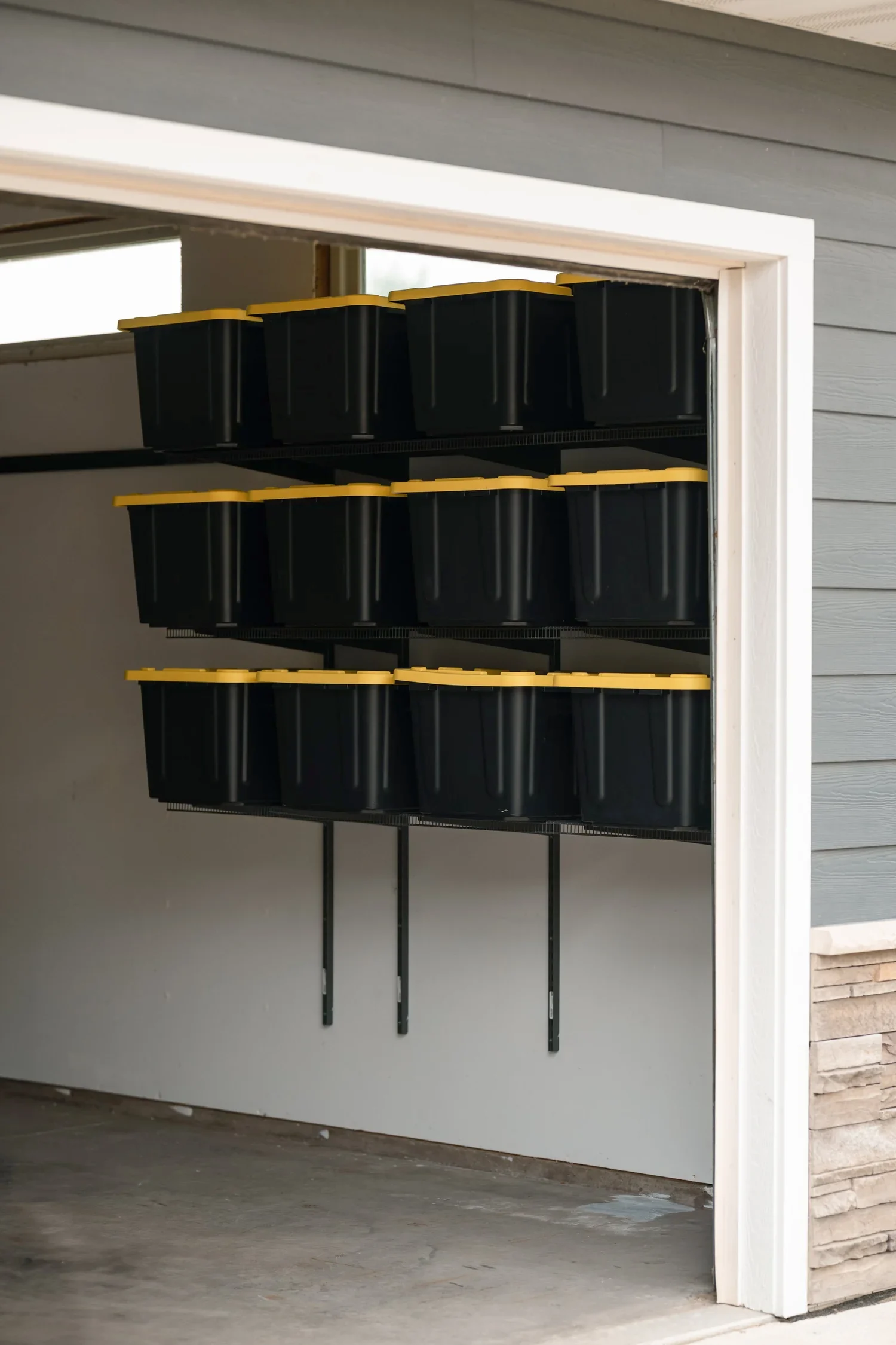 Storage bins on gunmetal garage shelves, seen through the garage door opening
