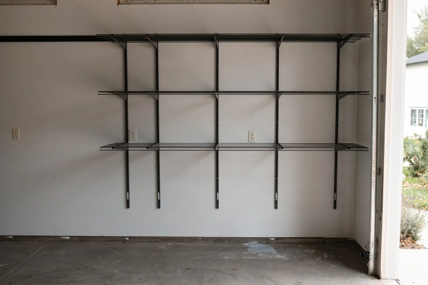 Empty gunmetal shelves on wall rails along a garage wall