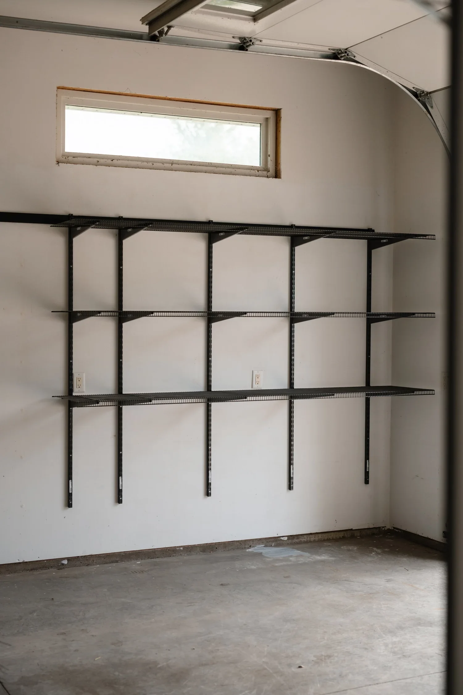 Empty gunmetal shelves on wall-mounted rails beneath a garage window