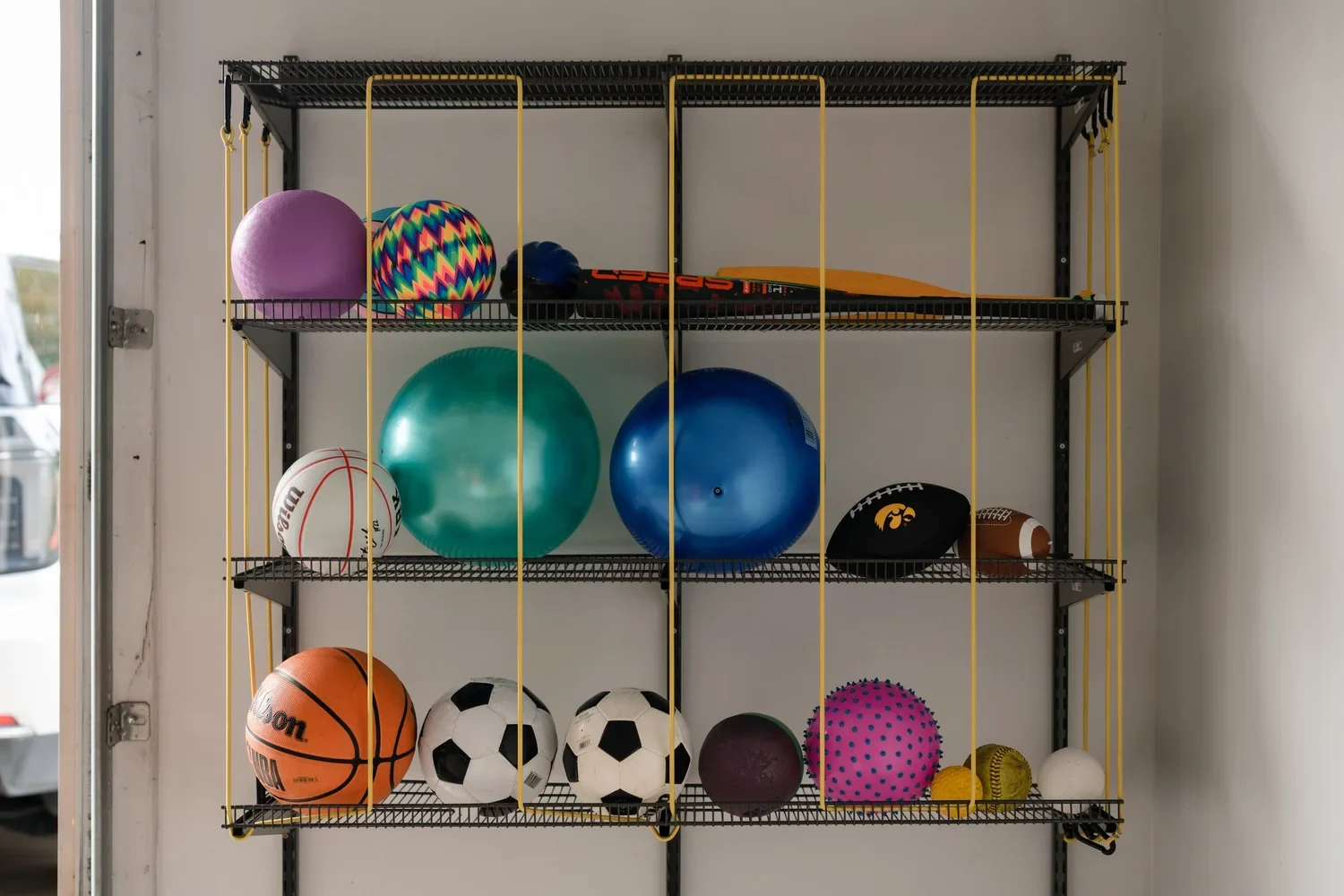 A full ball rack with yellow bungee cords on gunmetal garage rails, seen straight on