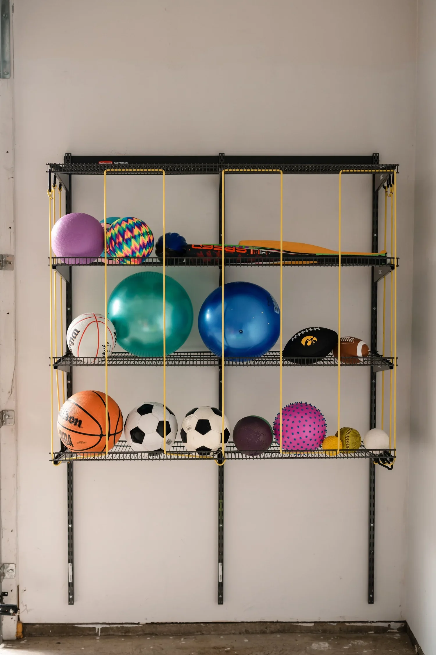 Gunmetal wire shelves on garage wall rails, with yellow bungee cords holding sports balls