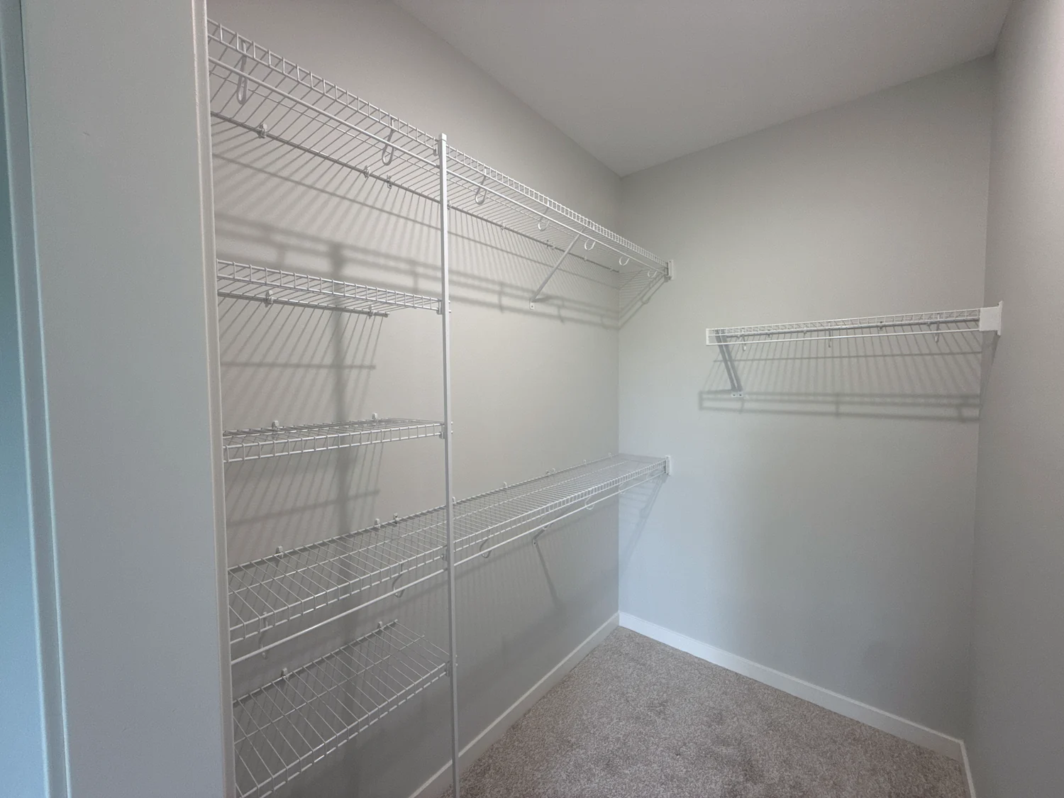 White wire shelving and hanging rods along two walls of an empty walk-in closet