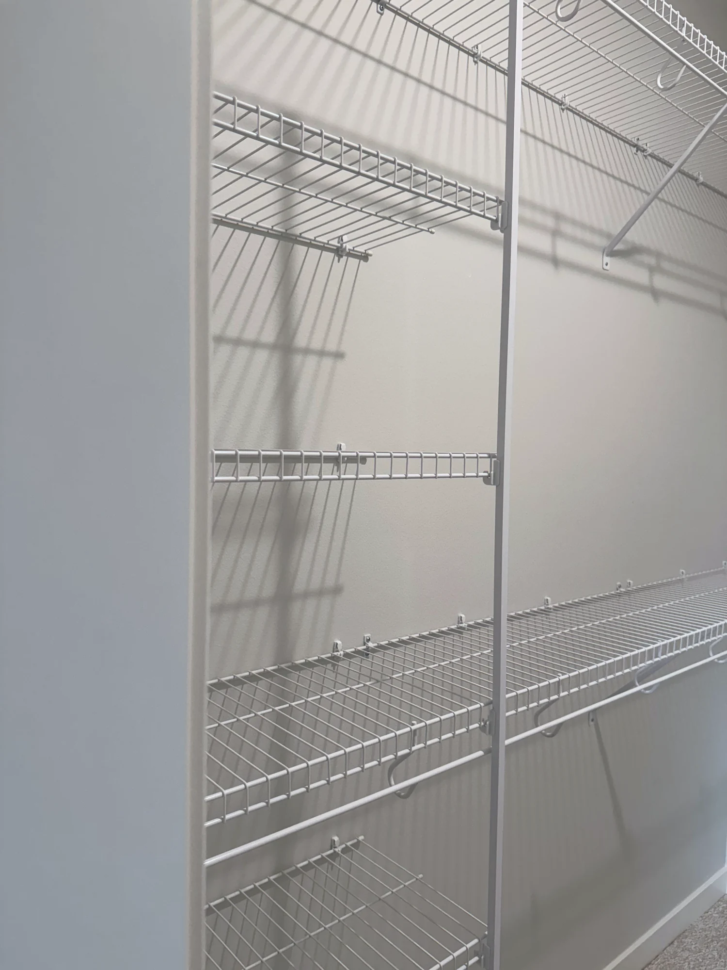 A wall of white wire shelves with hanging rods and a support pole in a walk-in closet
