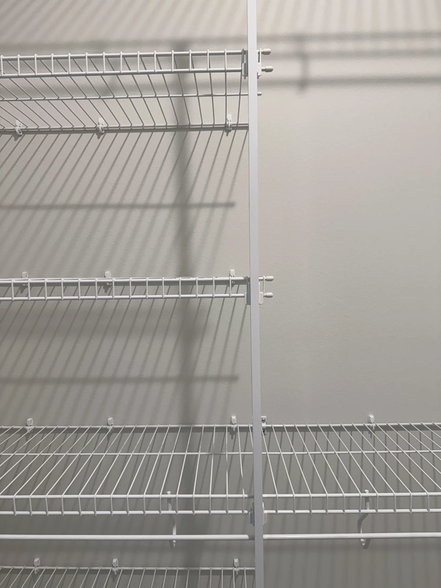 Straight-on view of white wire shelves with a support pole in a walk-in closet
