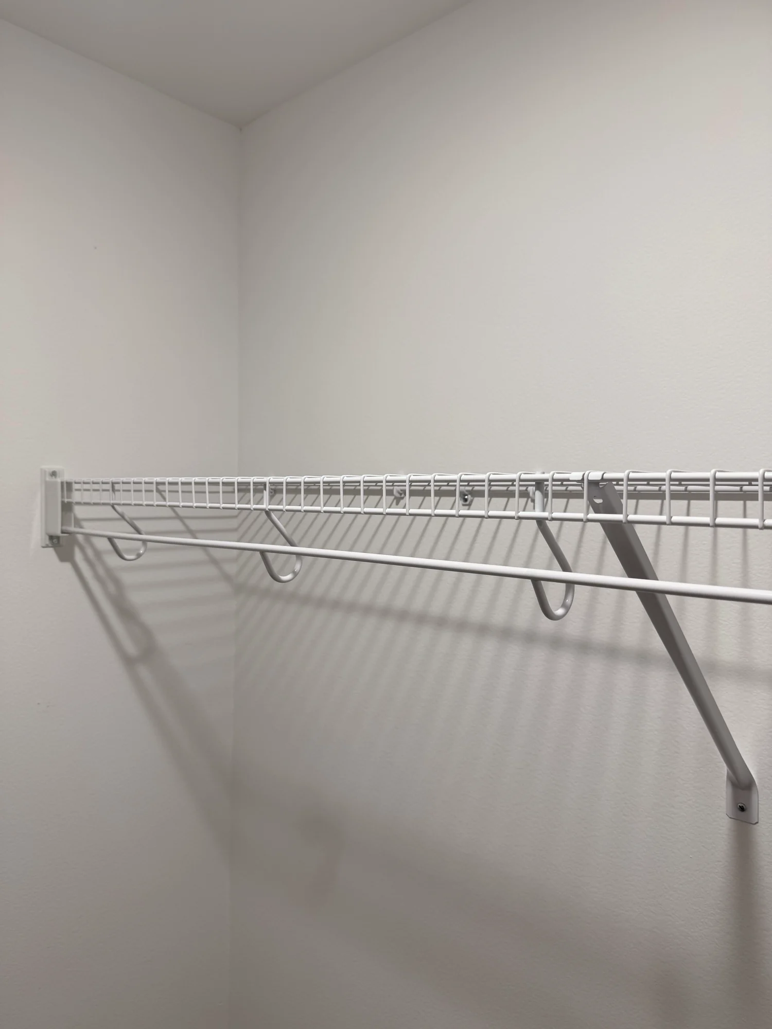 A single white wire shelf and hanging rod on a closet wall