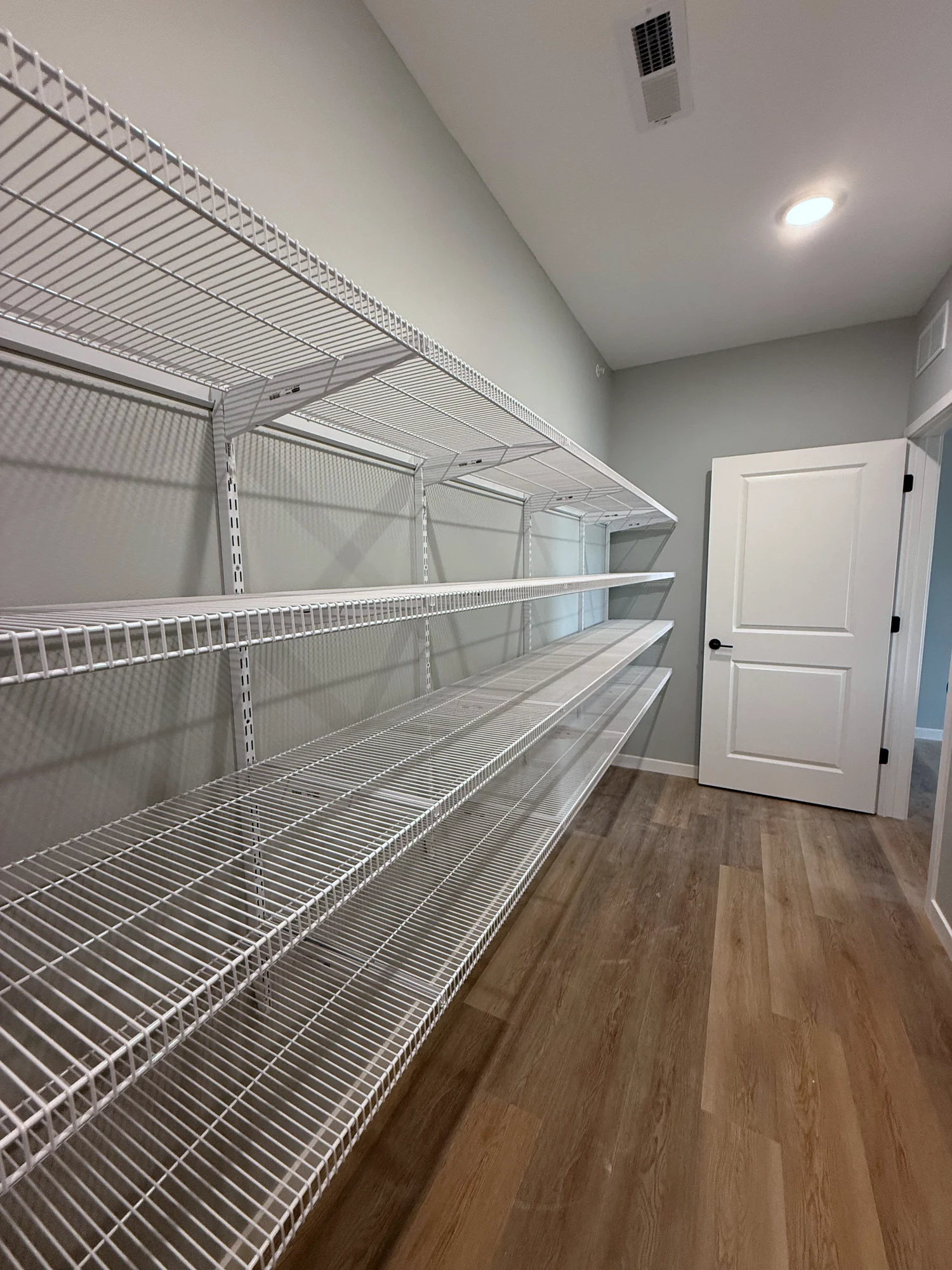 A walk-in pantry lined with white wire shelves on adjustable wall standards