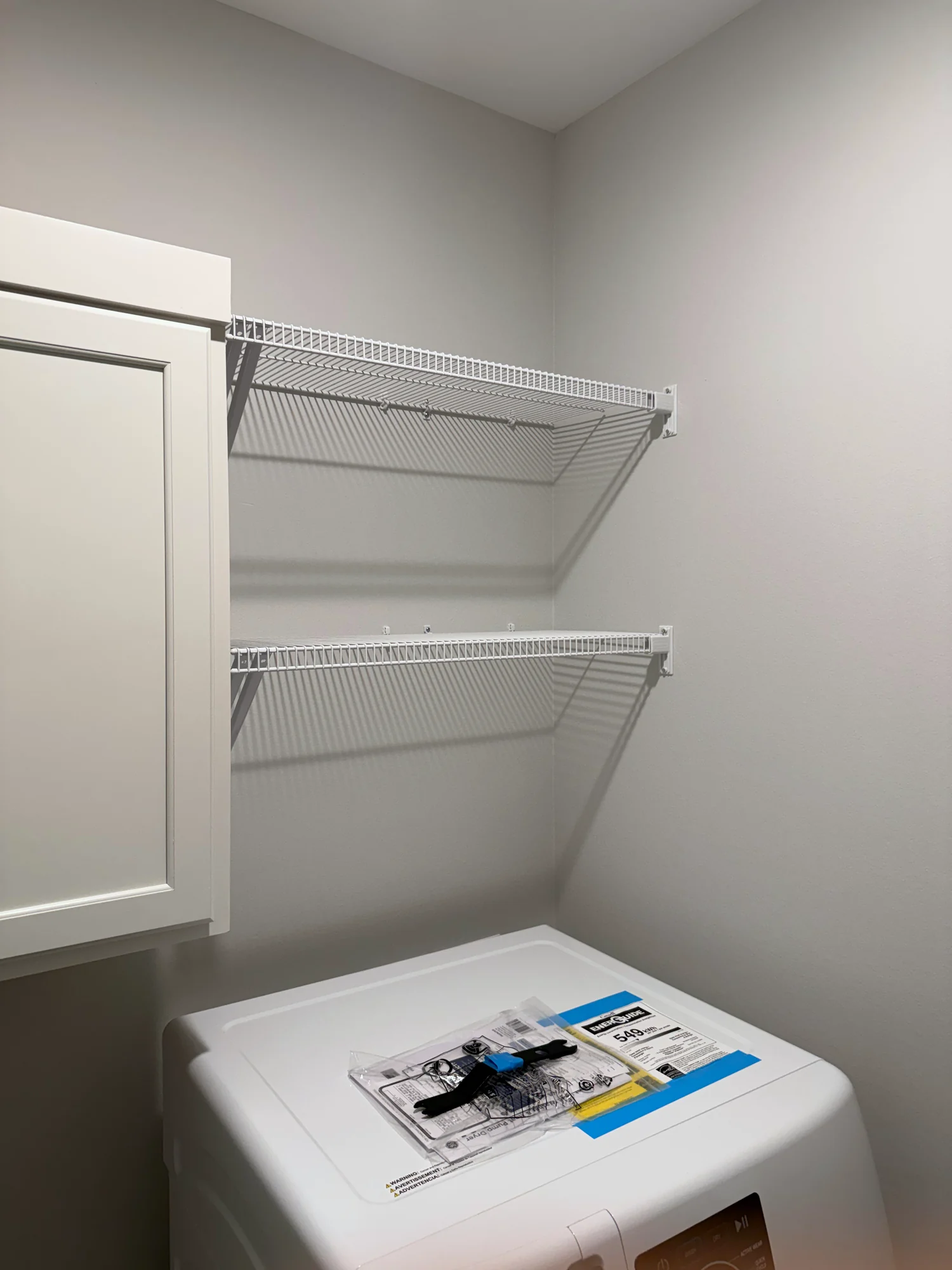 Two white wire shelves above a new washer in a laundry room