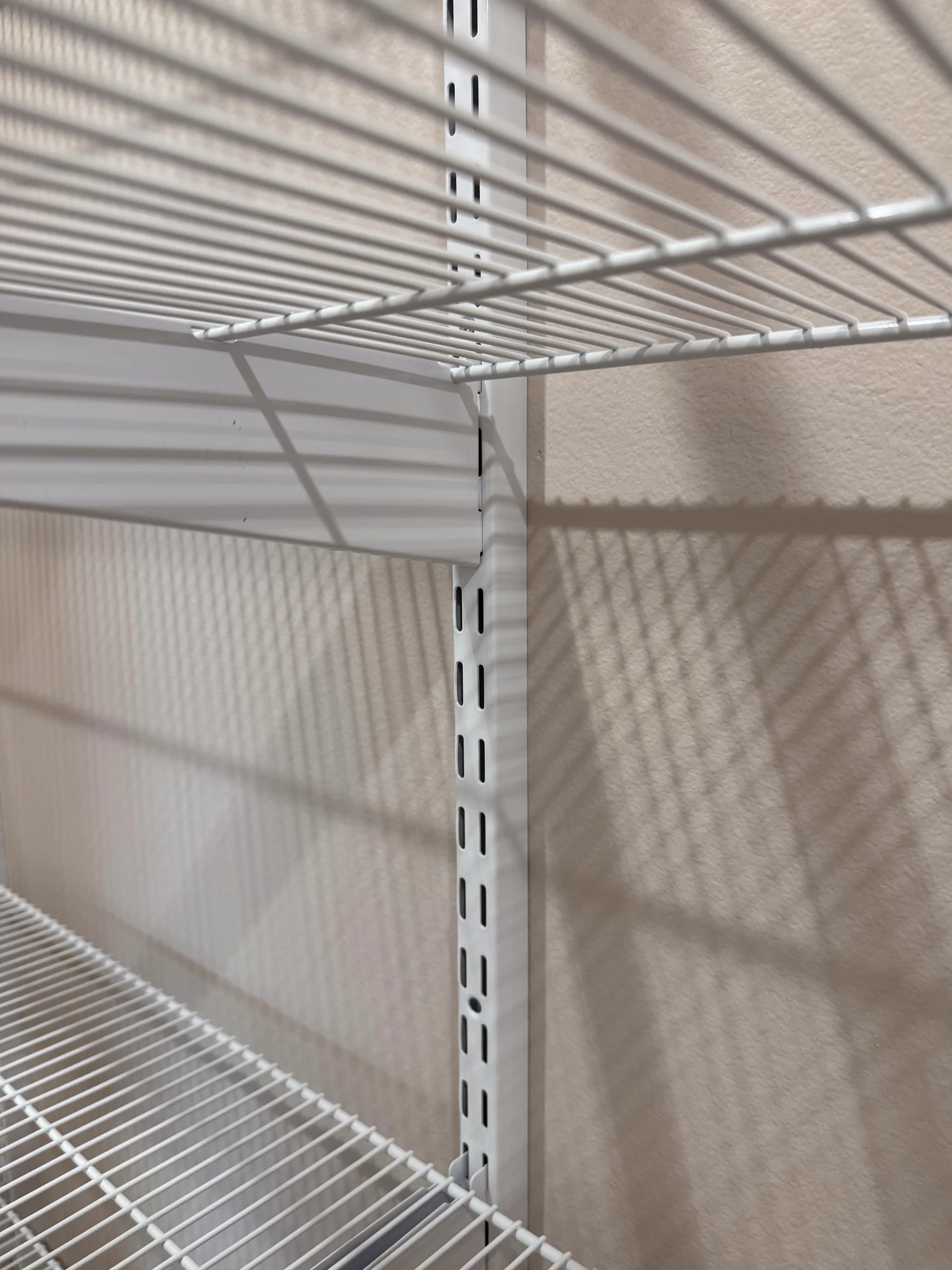Close view of a slotted wall standard and bracket holding white wire shelves